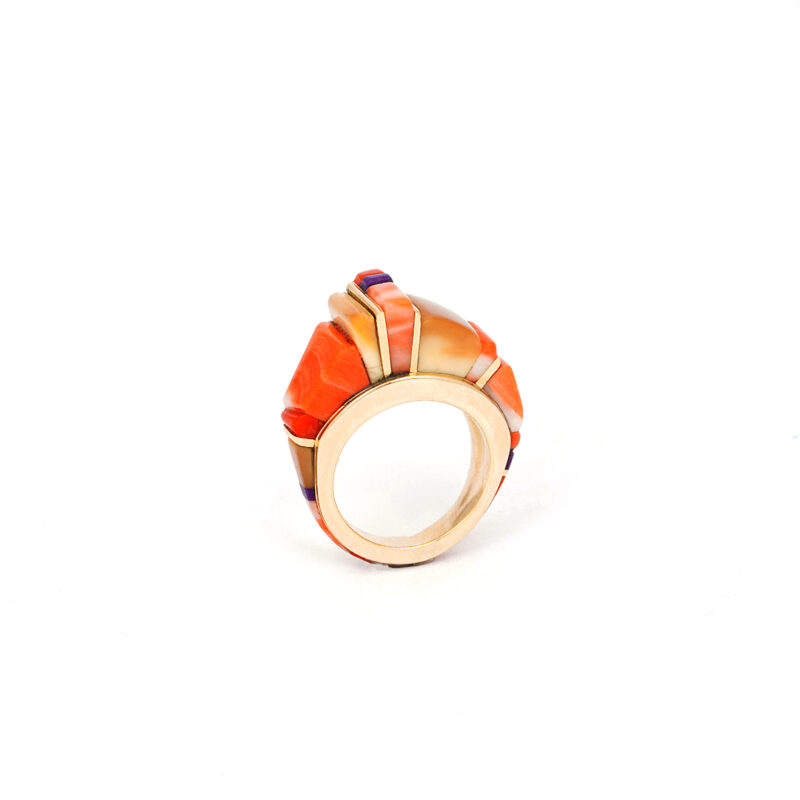 This ring is a powerful example of Charles Loloma’s visionary work. A true icon of Hopi contemporary jewelry, Loloma redefined Native art in the 20th century by blending traditional materials into modern style. The ring is made of 18k  gold and features inlaid stones consisting of pink coral, mediteranian coral, sugilite, fossilized ivory, and fine-line gold accent spacers wrapping around the entire gold frame. His bold color contrasts (like the orange and purple here) showed how Native jewelry was brought to a modern level of artistry. The elevated, tiered design is classic Charles Loloma—rising like a landscape of the Hopi Mesa.